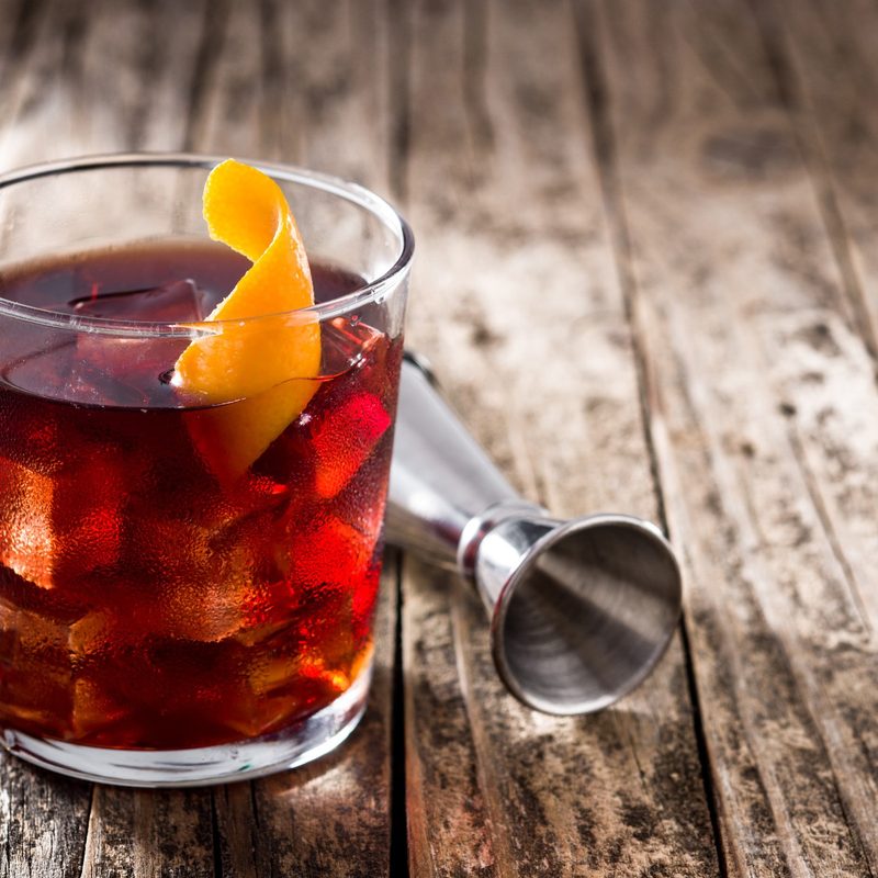 Boulevardier cocktail and orange zest on wooden table