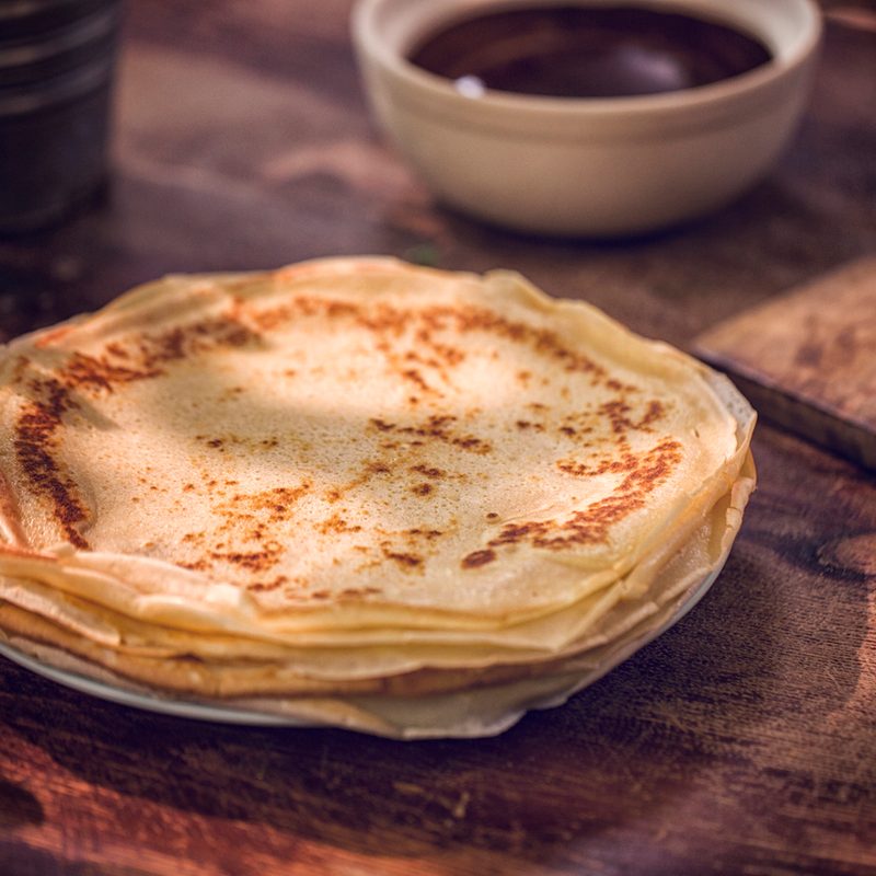 Preparing baked crepes pancakes with ham and tomatoes