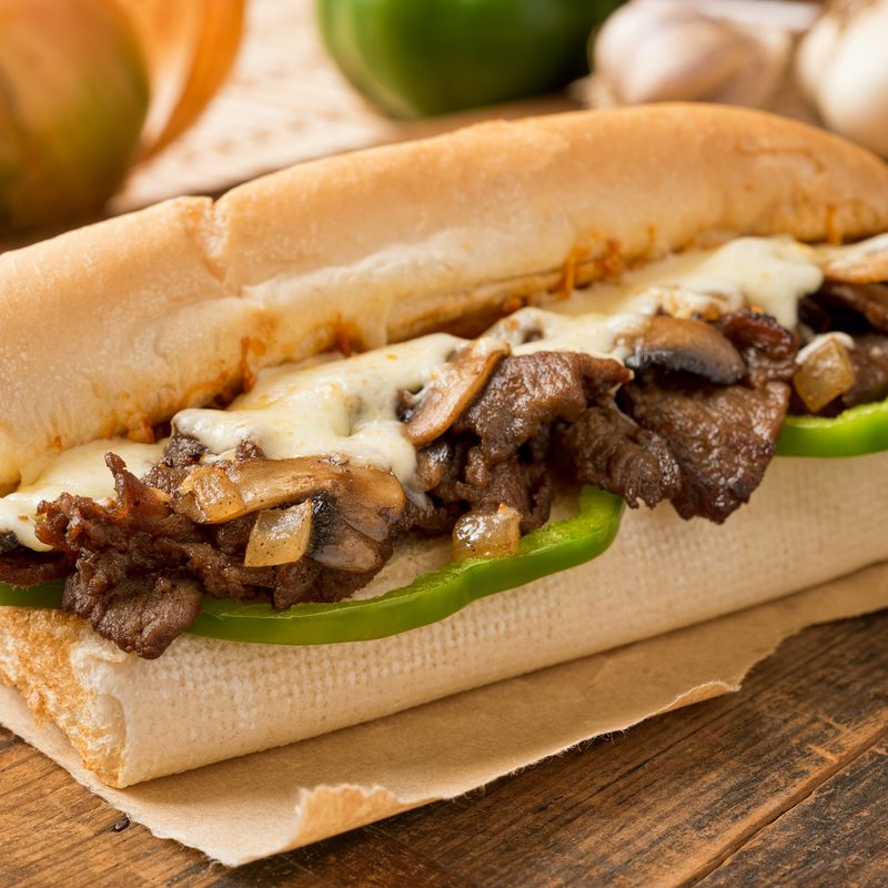 A delicious oven baked steak and cheese submarine sandwich with mushrooms, green peppers, and onion.