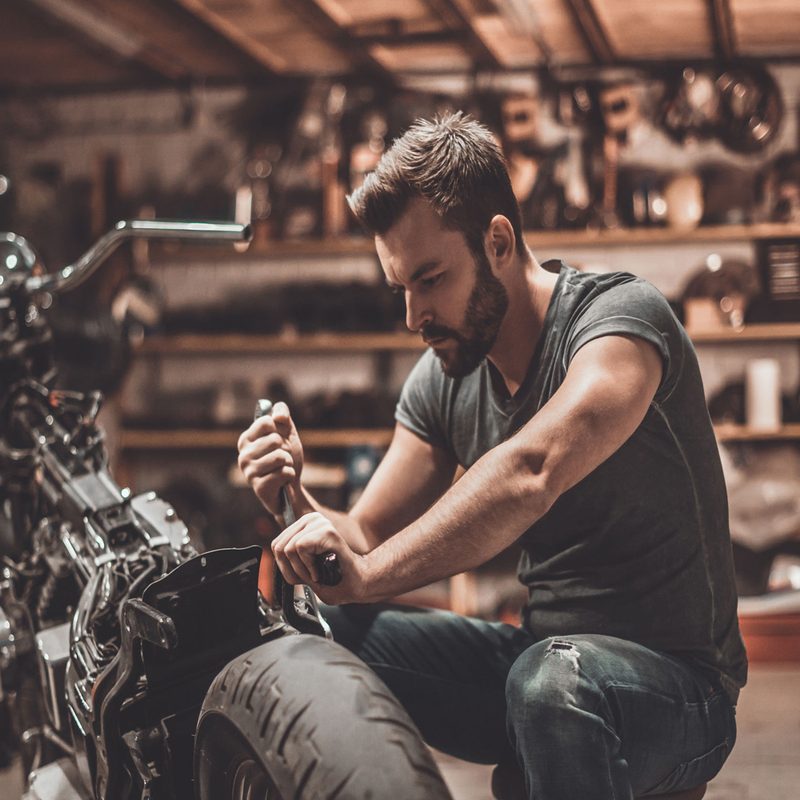 A fit man repairing his motorcycle.
