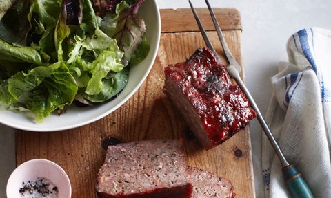 Overhead view of classic meatloaf and bowl of salad on cutting board