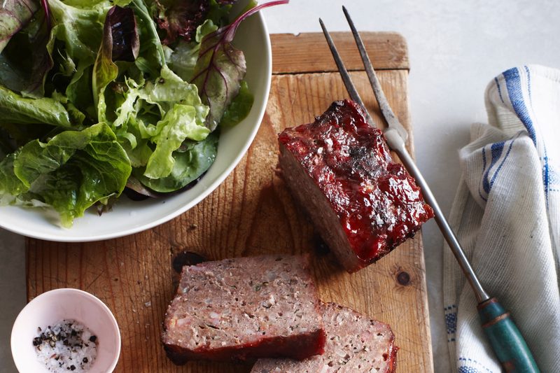 Overhead view of classic meatloaf and bowl of salad on cutting board