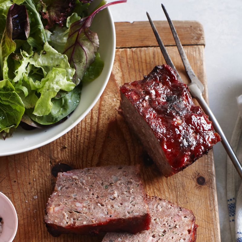 Overhead view of classic meatloaf and bowl of salad on cutting board