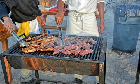 Two men grilling slabs of meat on a grill outdoors.