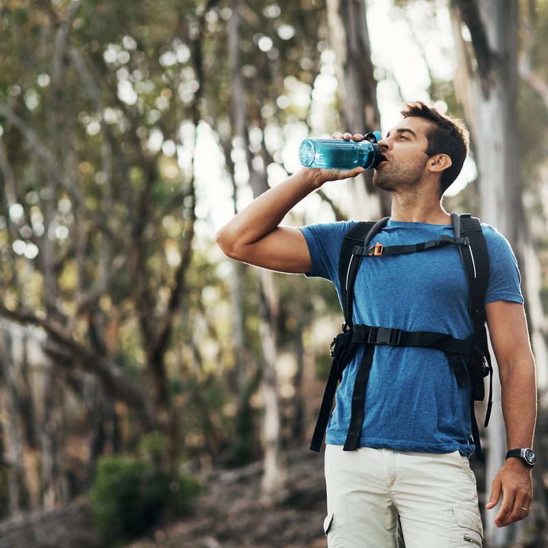 A carefree young man drinks water from a bottle while going for a hike up a mountain