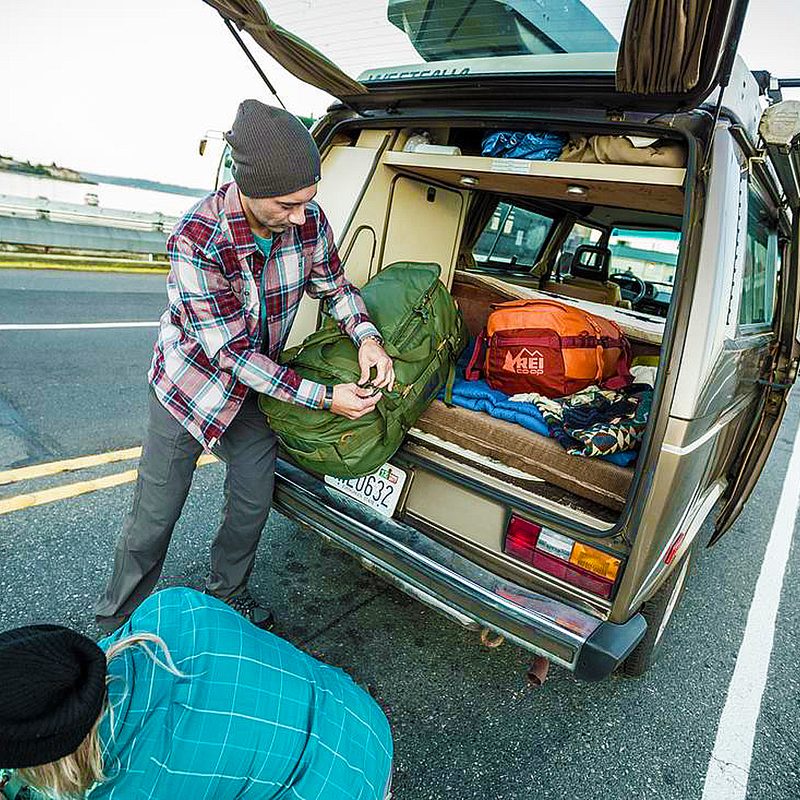 Man and woman preparing their REI camping gear in their van's trunk.