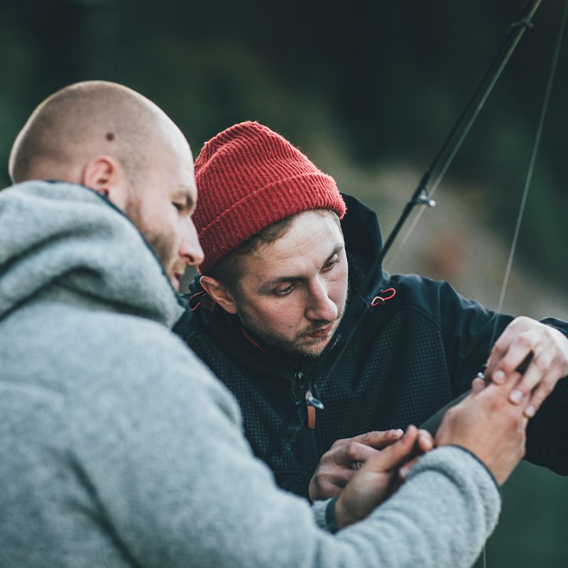 Young many helping his friend with a fishing rod
