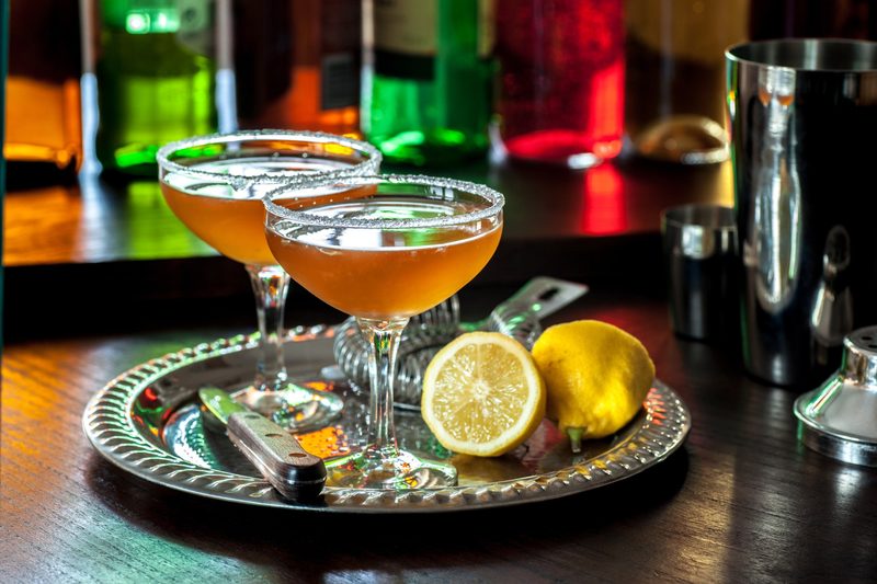 A pair of classic sidecar cocktails, served in vintage cocktail glasses with sugared rims, sitting on a vintage silver cocktail tray