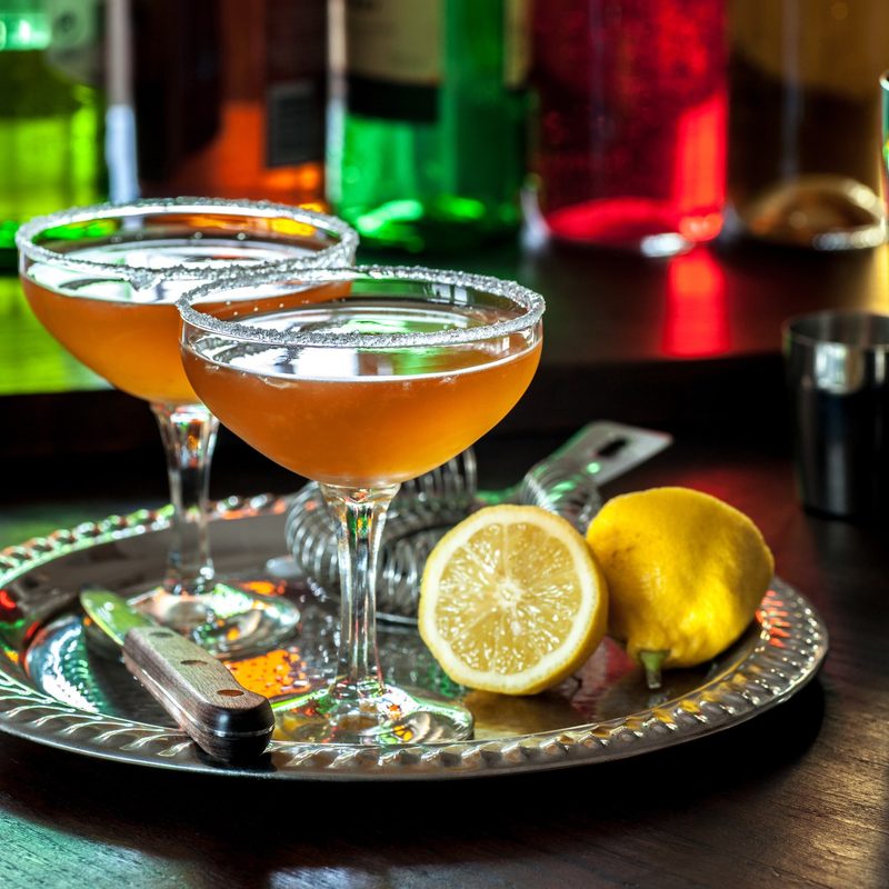 A pair of classic sidecar cocktails, served in vintage cocktail glasses with sugared rims, sitting on a vintage silver cocktail tray