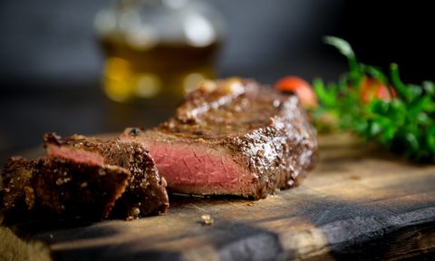 A plate of grilled meat and vegetables on a rustic wooden platter with a black background