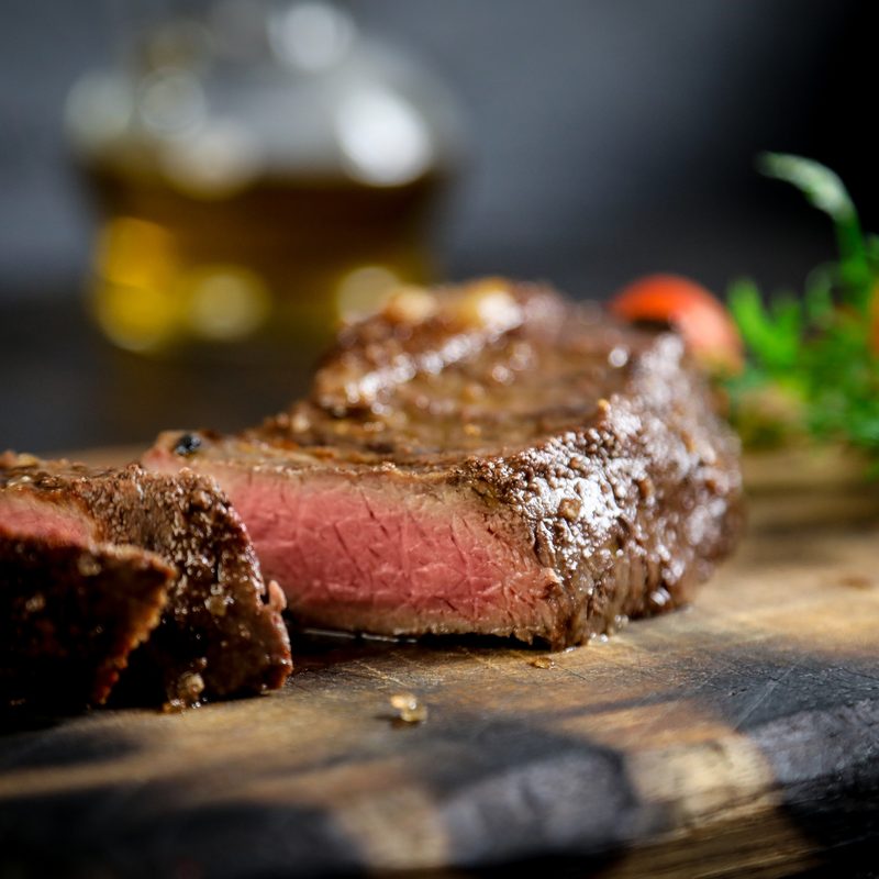 A plate of grilled meat and vegetables on a rustic wooden platter with a black background