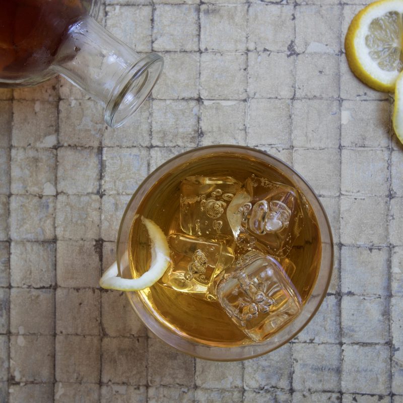 Classic Side Car cocktail garnished with lemon twist over ice with bottle and lemon slices