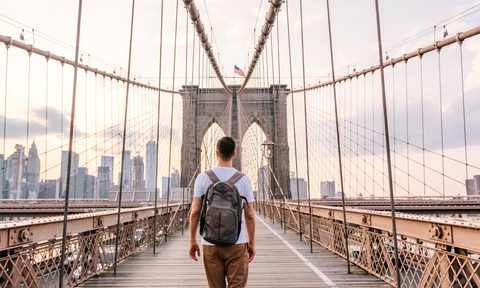 Rear view of a young man with backpack walking on Brooklyn Bridge, New York City, USA