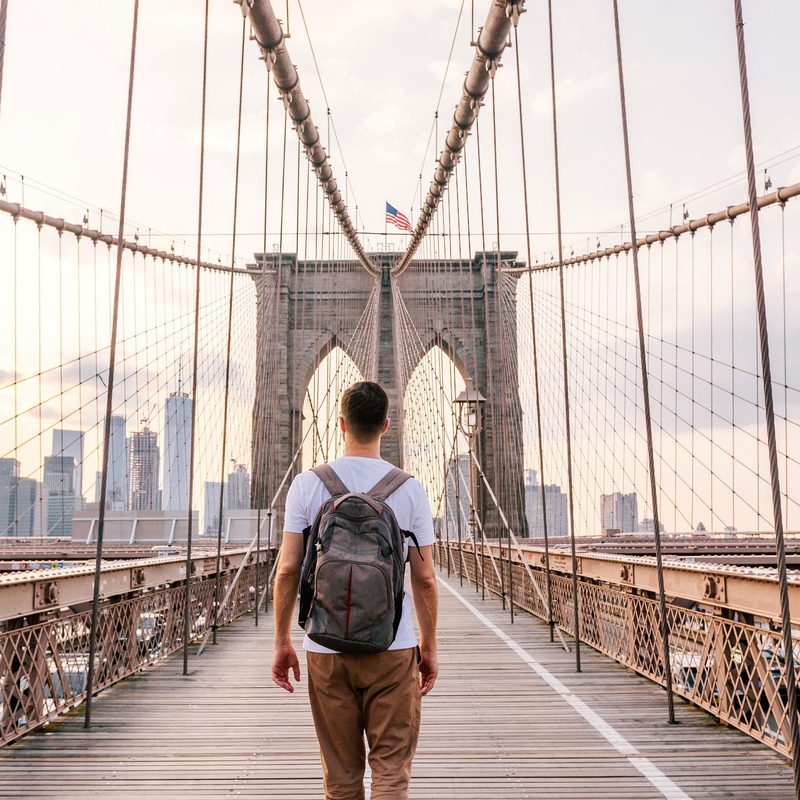 Rear view of a young man with backpack walking on Brooklyn Bridge, New York City, USA