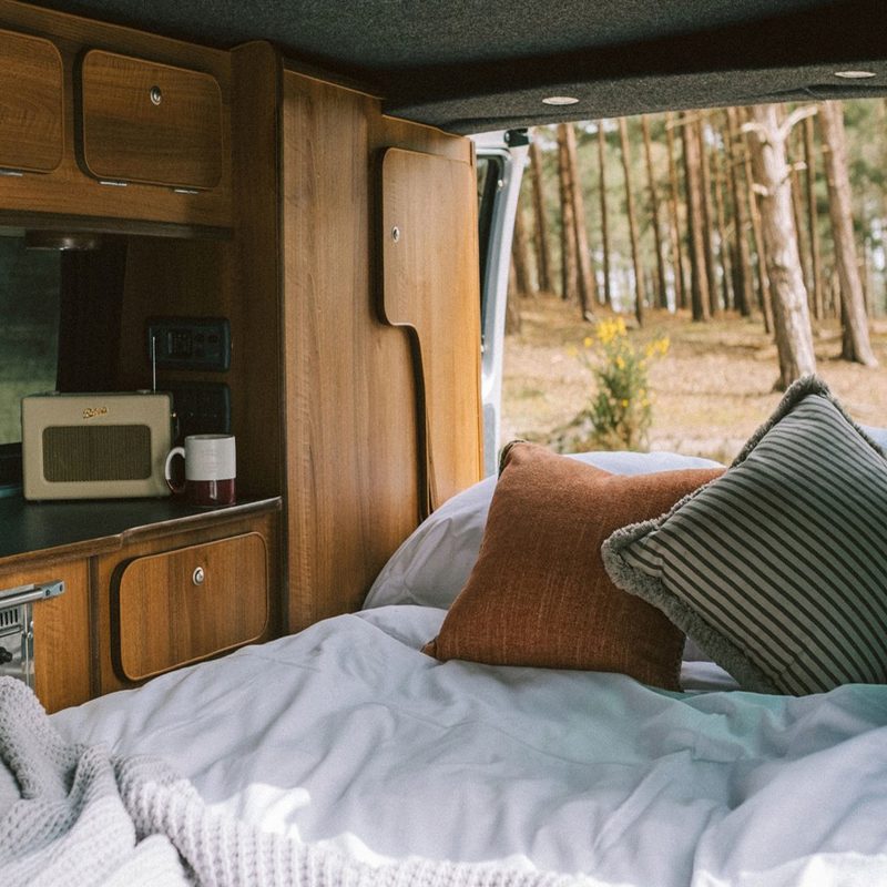 A bed with brown and black and white-striped pillows inside a camper van.
