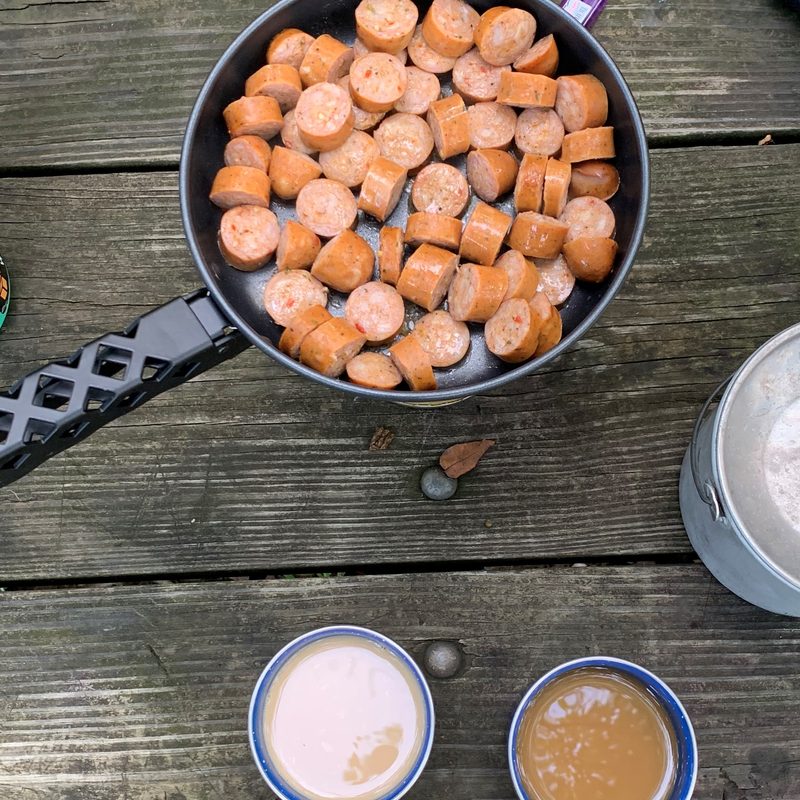 A camp table filled with camp stove, mugs, and other camping accessories.
