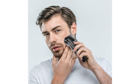 A close-up of a man shaving holding the electric razor to his face