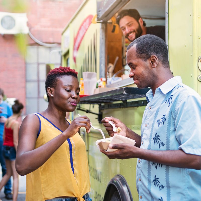 Couple eating lunch near a food truck.