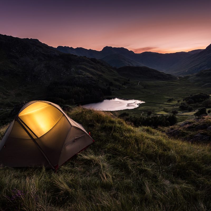 A lit-up tent overlooking the mountains at dusk.
