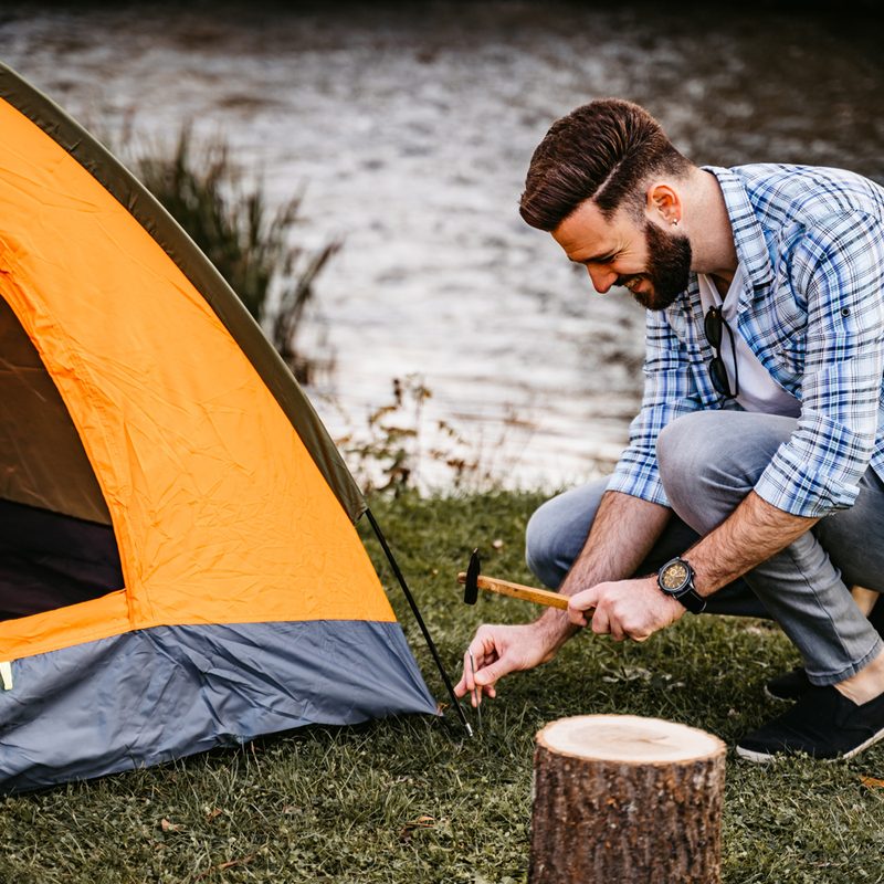 A man setting up a guyline for his tent.