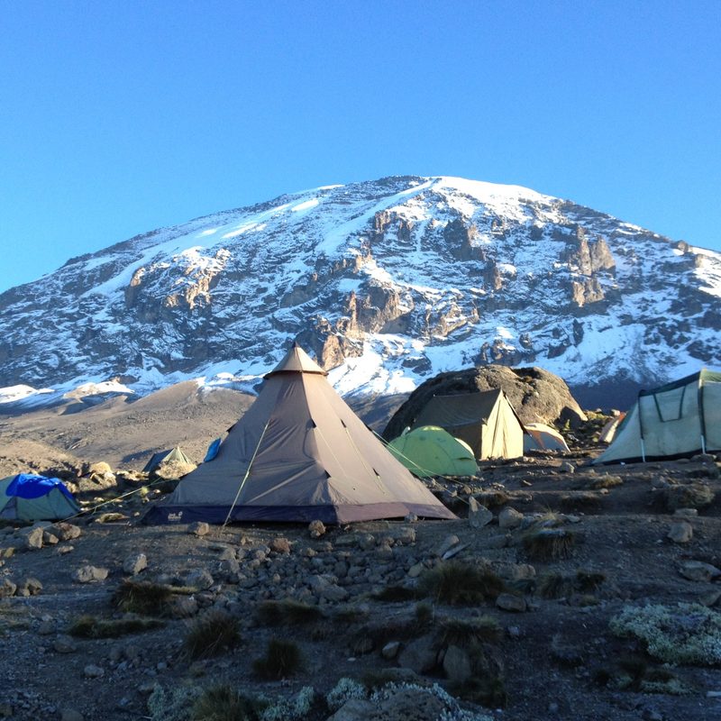 A selection of tents at the Karanga Camp with a snow topped mountain behind.