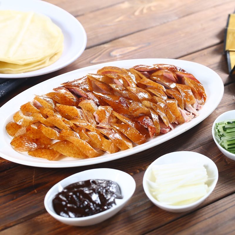 sliced Peking duck with garnishments sitting on a wooden table.