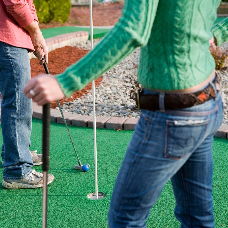 A lower body shot of a couple playing mini golf.