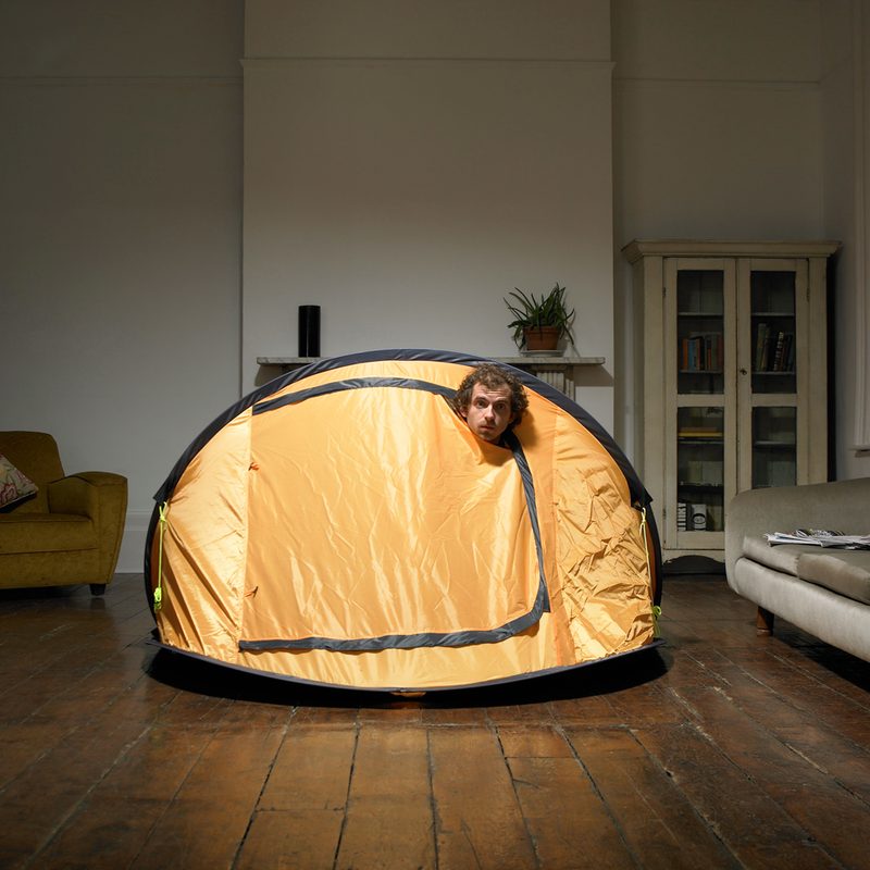 A man taking a peek from his yellow tent at home.