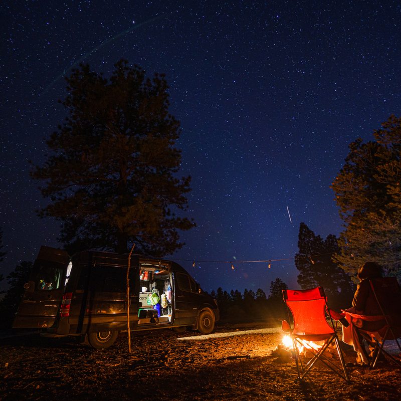 A vanlifer resting outside their converted Sprinter camper van at night.