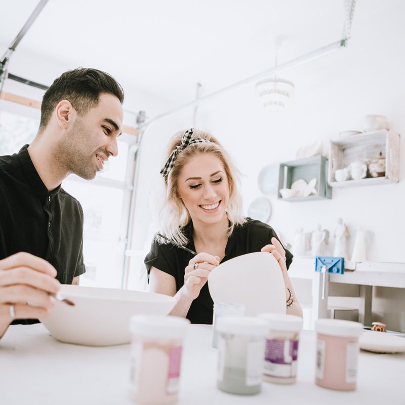 A couple painting their finished pottery pieces during art class.