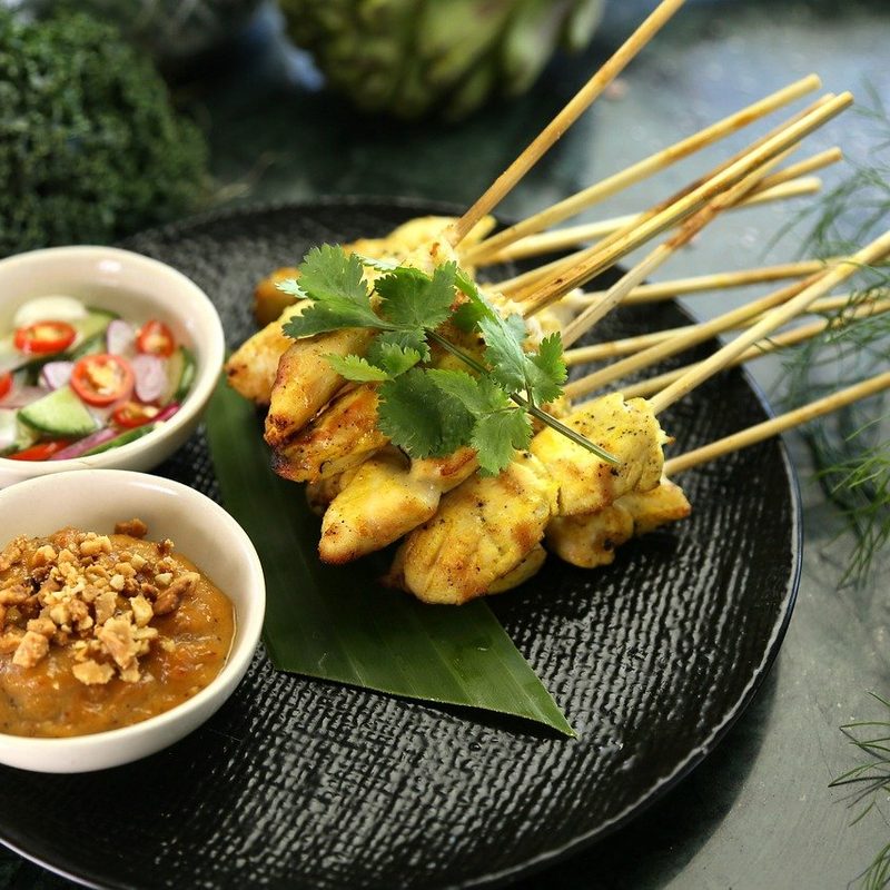 Thai Satay garnished with leaves served in a plate with sauces.