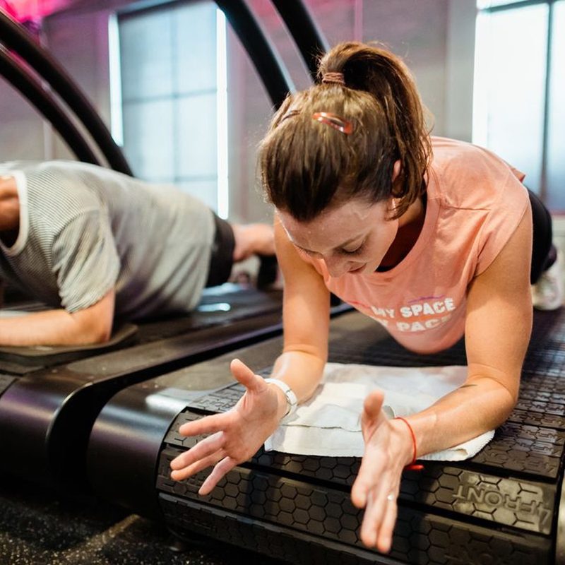 A man and a woman doing planks on treadmills at Stride Fitness