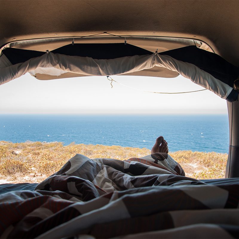 A first-person view of a tired adventurer enjoying the view of the sea from a van.