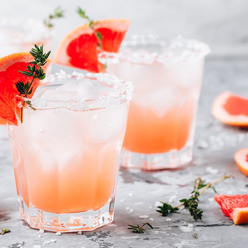 Grapefruit salty dog cocktail with ice in glass on gray stone background