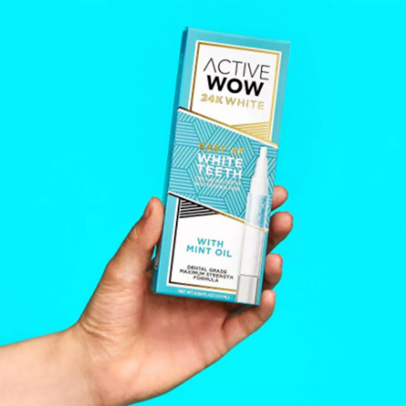 Hand holding Active Wow White Teeth Whitening Pen on teal background.