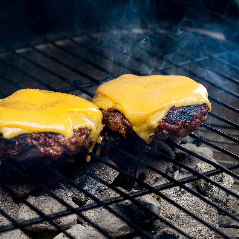 Melted American cheese topped on two charcoal grilled burgers.