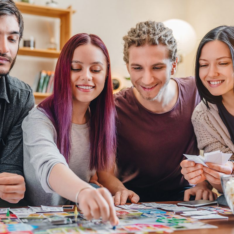Young group of friends playing board game on table at home interior.