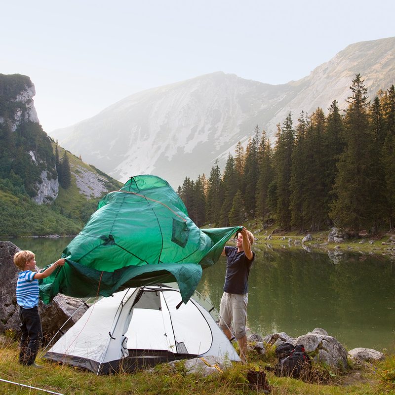 Father and son pitching a tent by a lake.