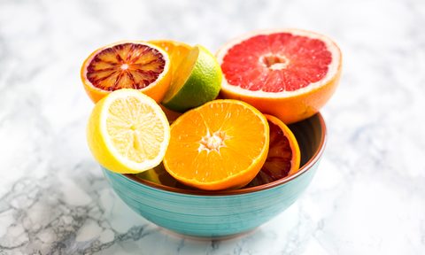 A teal bowl of citrus fruit on marble