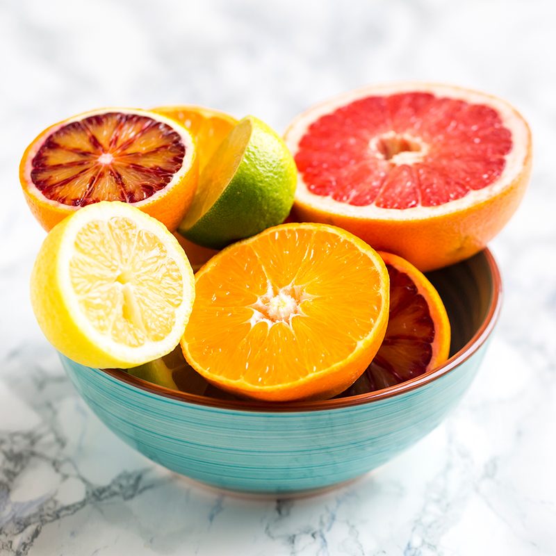 A teal bowl of citrus fruit on marble