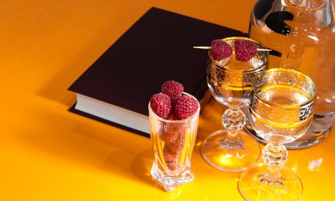 Black book surrounded by cocktail glassware in yellow background.