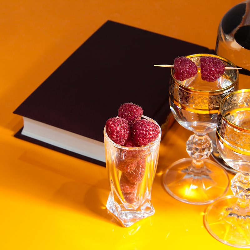 Black book surrounded by cocktail glassware in yellow background.