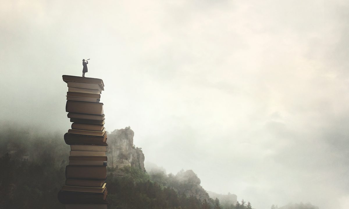 surreal man with telescope looks at infinity from the top of a stack of books in the outdoors.