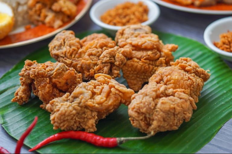 Fried chicken served on a leaf with a chili.