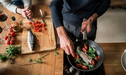 Mid section of young couple preparing fish at kitchen counter.