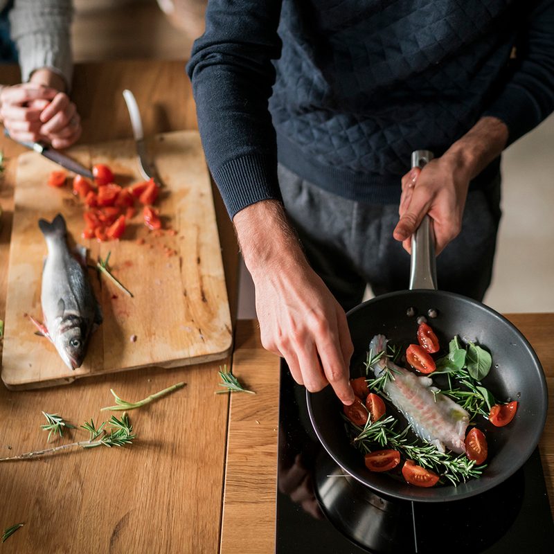 Mid section of young couple preparing fish at kitchen counter.
