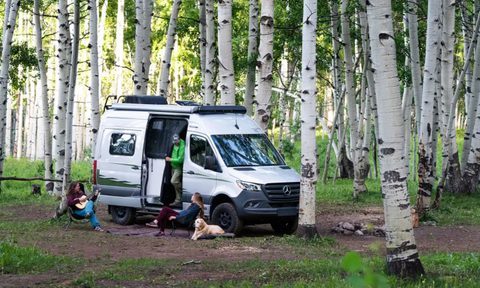 Three campers and a dog relaxing at a wilderness campsite with a Winnebago Revel campervan.