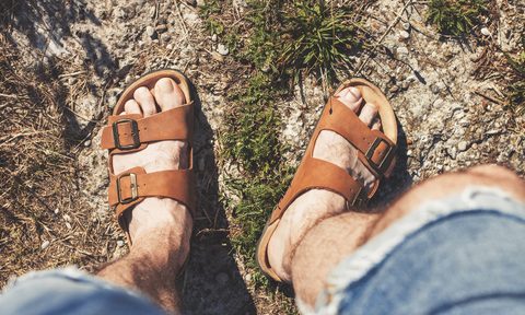 Downward view of a man's feet wearing brown sandals standing on grass.