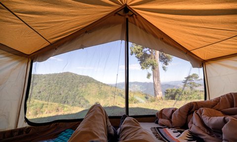 A first-person view of a man relaxing in a tent on a hill.