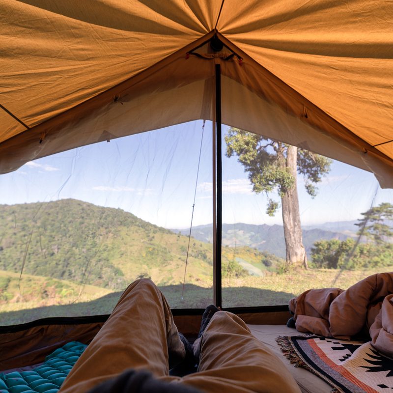 A first-person view of a man relaxing in a tent on a hill.
